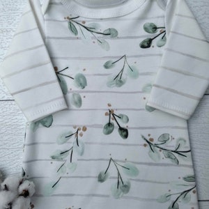 May include: White baby sleeper with long sleeves and a round neckline. The sleeper features a pattern of green eucalyptus leaves and brown accents on a white background with gray horizontal stripes.