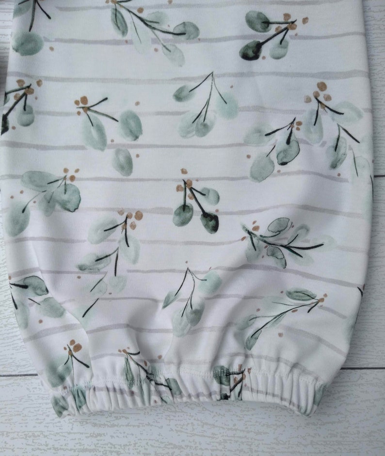 May include: White baby gown with a watercolor eucalyptus leaf pattern in shades of green and brown. The gown features horizontal gray stripes and an elasticated bottom hem. The fabric is soft and appears to be cotton.