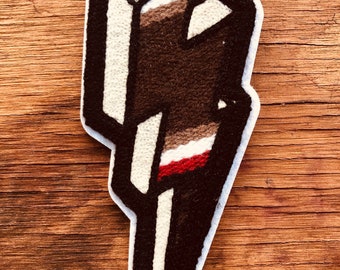 May include: A brown, white, and red embroidered lightning bolt patch. The patch is made of felt and has a white outline.