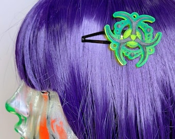 May include: A black metal hair clip featuring a neon green and dark gray biohazard symbol design. The accessory is attached to straight, vibrant purple hair, showcasing a circular, layered structure with cut-out details and a bright green center.