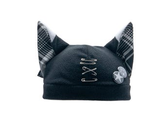 May include: Black fleece beanie hat with cat ears. The ears have a black and white plaid pattern. The hat is decorated with safety pins and two small star-shaped pins.