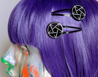 May include: Two black metal hair clips, each featuring a circular charm with a silver-toned pentagram design. The clips are positioned on vibrant purple hair, showcasing a sleek, dark aesthetic with clear, sharp lines on the star emblems.