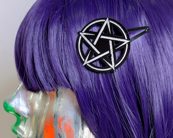 May include: A black hair clip featuring a circular pentagram design with white outlines. The accessory is attached to vibrant purple hair. The pentagram is centered within a circular frame, and the clip mechanism extends from the side of the circular shape.