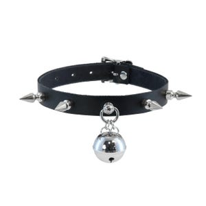 Könnte beinhalten: Schwarze Leder-Halskette mit silberfarbenen Kegel-Nieten und einer hängenden silbernen Glocke. Die Halskette hat einen Schnallenverschluss und einen silberfarbenen Metallring.
