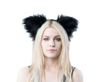 May include: Black faux fur cat ears headband. The ears are fluffy and stand upright on a black headband. The accessory is worn on a person with long blonde hair and blue eyes, against a white background.