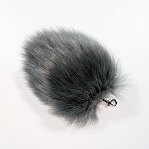 May include: A fluffy, gray faux fur accessory with a silver-colored metal clasp. The fur is a mix of dark and light gray, creating a textured appearance. The clasp is attached to the fur, suggesting it can be clipped onto something.