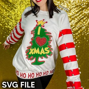May include: White Christmas sweatshirt with a green Christmas tree design, a red heart, and the text "I XMAS". The sleeves have red and white stripes with silver embellishments. The bottom of the sweatshirt has the text "HO HO HO".