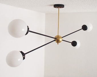May include: A modern black and gold chandelier with four white globe-shaped light fixtures. The chandelier has a geometric design with arms extending from a central point.