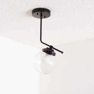 May include: A black ceiling light fixture with a single globe-shaped glass shade. The fixture has a long, straight arm that extends out from the ceiling mount and then bends at a 90-degree angle.
