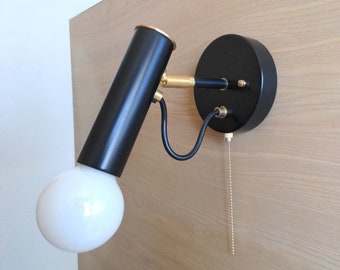 May include: Black wall-mounted light fixture with a white globe and a brass pull chain. The light fixture has a cylindrical shade and a round base.