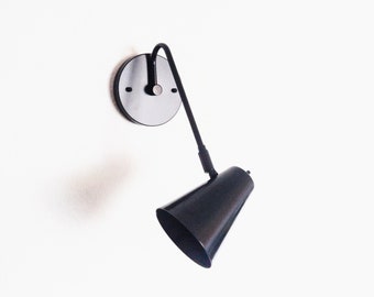 May include: Black wall-mounted light fixture with a round base and a long, adjustable arm. The light has a black, cone-shaped shade.