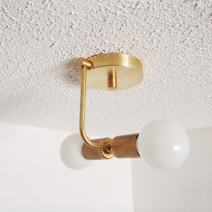 Puede incluir: Una lámpara de techo dorada con dos bombillas blancas esféricas. La lámpara tiene un diseño simple y moderno.