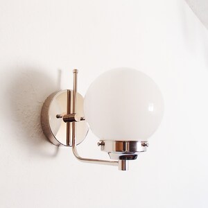 Peut inclure: Une applique murale chrom&eacute;e avec un luminaire blanc en forme de globe.