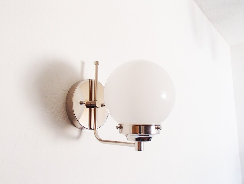 Peut inclure: Une applique murale chrom&eacute;e avec un luminaire blanc en forme de globe.