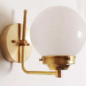 Peut inclure: Une applique murale en laiton avec un abat-jour en globe blanc. L'applique a un design simple et moderne et est parfaite pour ajouter une touche d'&eacute;l&eacute;gance &agrave; n'importe quelle pi&egrave;ce.