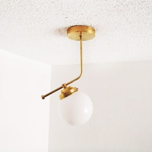 May include: A gold ceiling light fixture with a white globe shade. The light fixture has a curved arm that extends out from the center.