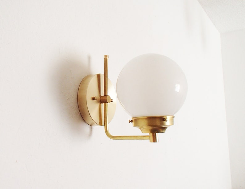 Peut inclure: Une applique murale en laiton avec un abat-jour en verre blanc rond. L'applique a un design simple et moderne.