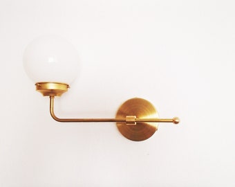 May include: A brass wall sconce with a white globe shade. The sconce has a curved arm and a round base.