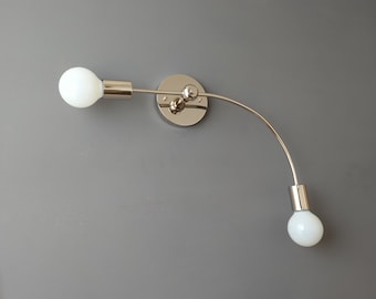 May include: A chrome wall sconce with two white globe light bulbs. The sconce has a curved arm that extends out from the wall.