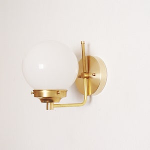 Peut inclure: Une applique murale en laiton avec un abat-jour en globe blanc. L'applique a un design simple et moderne et est parfaite pour ajouter une touche d'&eacute;l&eacute;gance &agrave; n'importe quelle pi&egrave;ce.