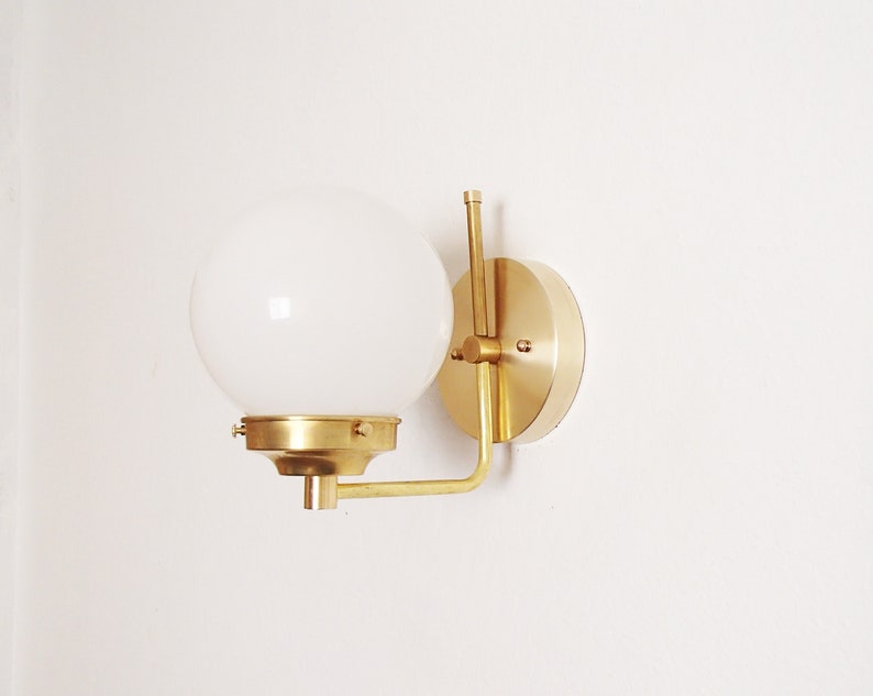 Peut inclure: Une applique murale en laiton avec un abat-jour en globe blanc. L'applique a un design simple et moderne et est parfaite pour ajouter une touche d'&eacute;l&eacute;gance &agrave; n'importe quelle pi&egrave;ce.