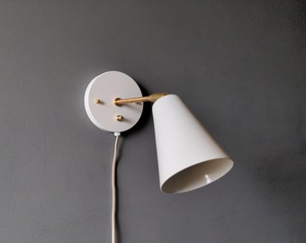 May include: White wall-mounted light fixture with a cone-shaped shade and a brass arm. The fixture has a white cord.