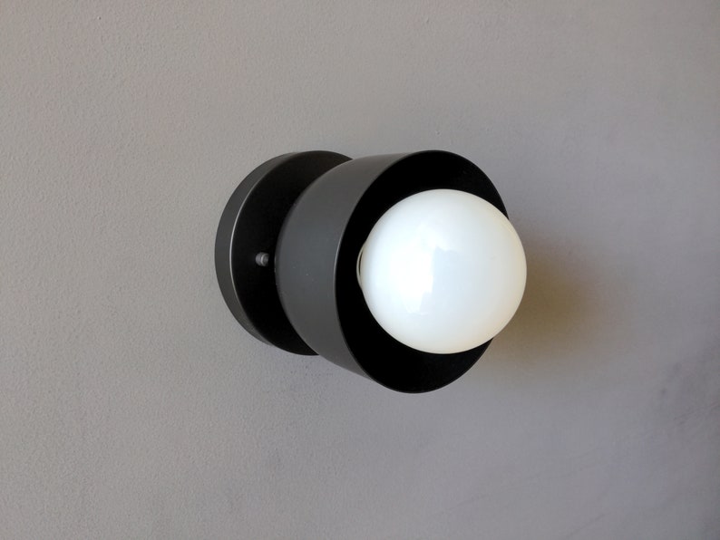 A modern and minimalist style wall sconce with half spherical shaped shade, flat wall base, dark oil rubbed bronze finish, white globe bulb. Gray background.