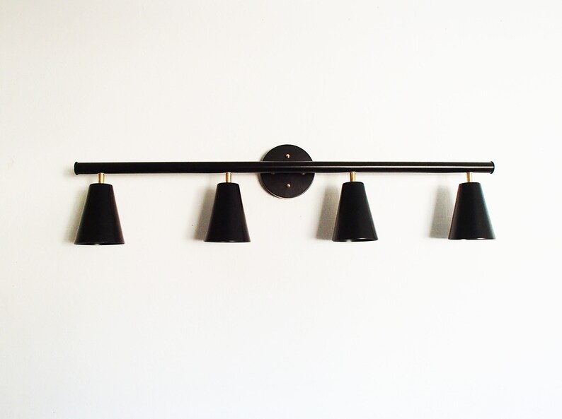 May include: Black metal light fixture with four black cone-shaped shades. The fixture is mounted to a wall and has a circular base.