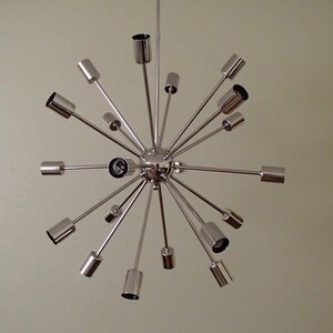 May include: A chrome Sputnik chandelier with multiple arms extending outward from a central sphere. The chandelier has a modern, mid-century design.