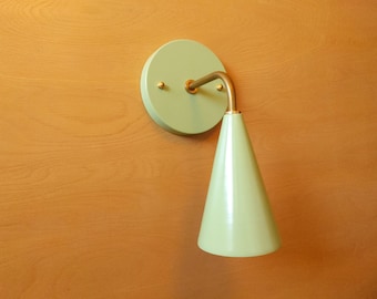 May include: A light green wall sconce with a cone-shaped shade and a round base. The sconce has a brass arm and a brass mounting plate.