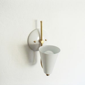 Puede incluir: Aplique de pared blanca con un brazo de lat&oacute;n y una pantalla c&oacute;nica blanca.