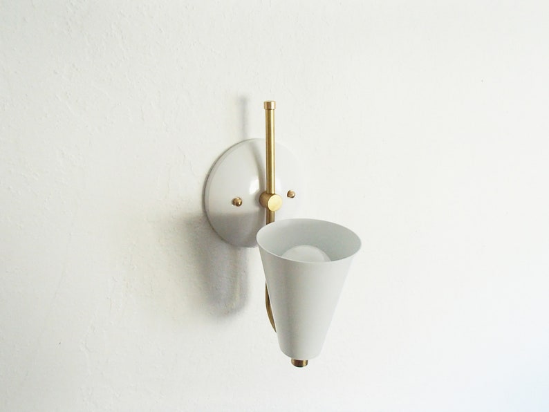 Puede incluir: Aplique de pared blanca con un brazo de lat&oacute;n y una pantalla c&oacute;nica blanca.