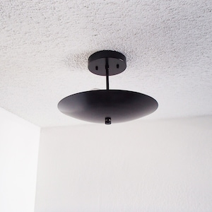 Peut inclure: Un luminaire de plafond noir avec un abat-jour rond et plat.