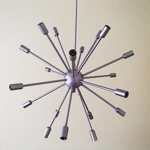 May include: A silver metal Sputnik chandelier with multiple arms extending outward from a central sphere. The chandelier has a modern, mid-century design.