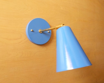 May include: A blue wall sconce with a cone-shaped shade. The sconce has a brass arm and a round base.