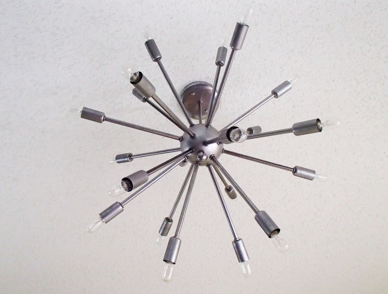 May include: A silver metal Sputnik style chandelier with multiple arms extending outward from a central sphere. Each arm has a light bulb at the end.
