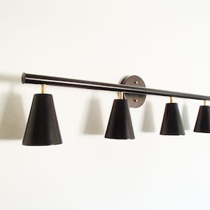 May include: A black metal light fixture with four black cone-shaped shades. The fixture has a round base and is mounted to a wall.