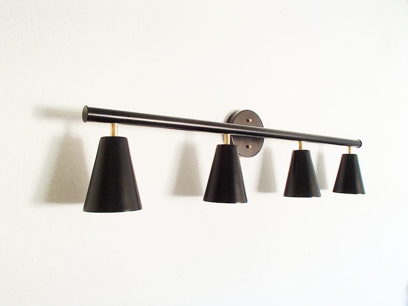 May include: A black metal light fixture with four black cone-shaped shades. The fixture has a round base and is mounted to a wall.