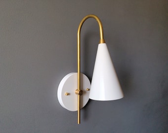 May include: A white cone-shaped lampshade with a gold metal arm and base. The lamp is mounted on a white circular wall plate.
