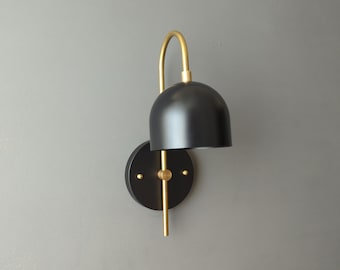 May include: Black and gold wall sconce with a dome-shaped shade. The sconce has a simple, modern design.