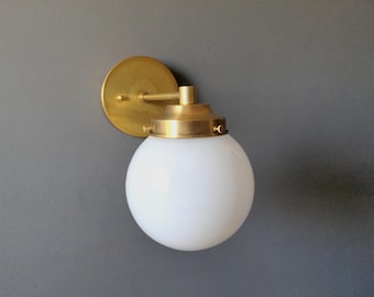 May include: A brass wall sconce with a white globe shade. The sconce has a round back plate and a simple arm.