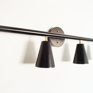 May include: A black metal light fixture with four black cone-shaped shades. The fixture is mounted to a wall and has a round base.