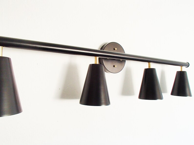 May include: A black metal light fixture with four black cone-shaped shades. The fixture is mounted to a wall and has a round base.