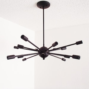Puede incluir: Candelabro de metal negro con un centro esférico y múltiples brazos que se extienden hacia afuera, cada uno terminando en una luminaria cilíndrica.