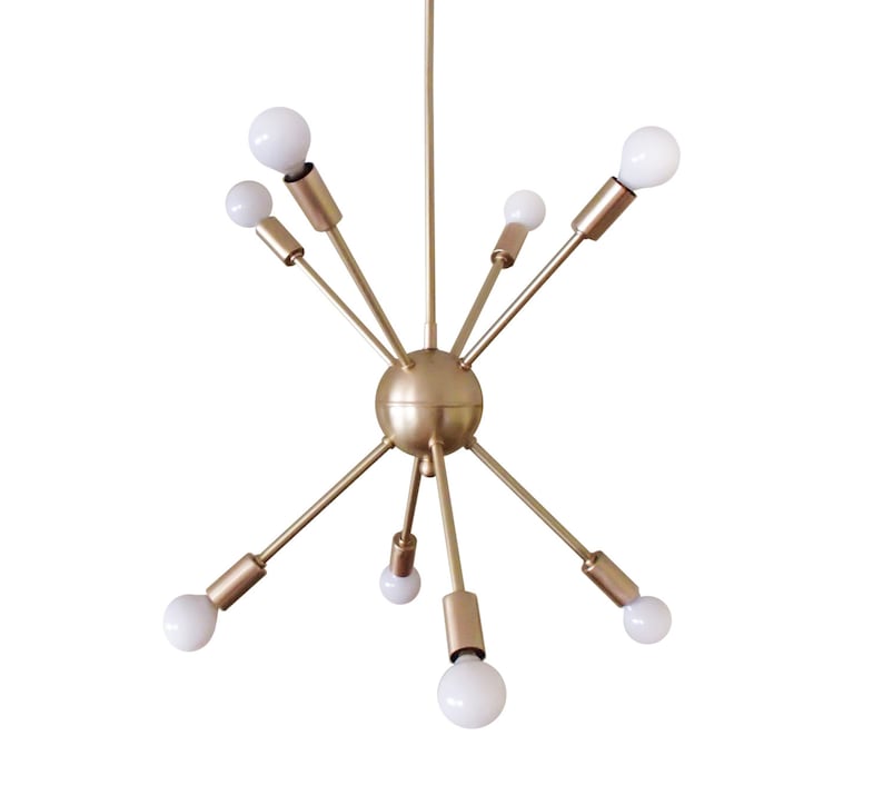 May include: A gold-toned, mid-century modern chandelier with eight light bulbs. The chandelier has a spherical center and six arms extending outward.