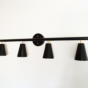 May include: Black four-light vanity light fixture with black cone-shaped shades. The fixture has a long, straight bar with a round base.