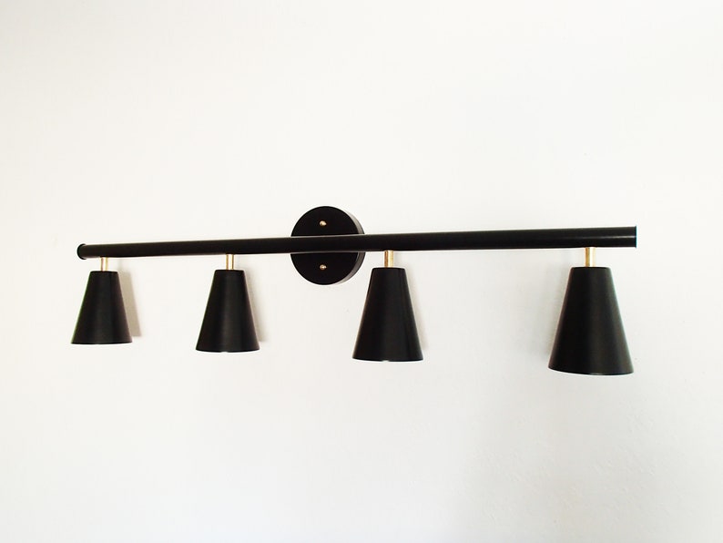 May include: Black four-light vanity light fixture with black cone-shaped shades. The fixture has a long, straight bar with a round base.