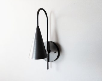 May include: A black metal wall sconce with a cone-shaped shade. The sconce has a simple, modern design.