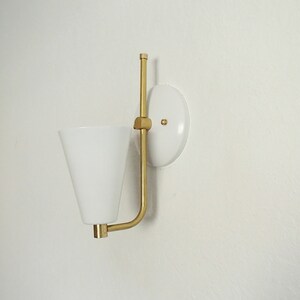 Puede incluir: Una l&aacute;mpara de pared blanca con un brazo de metal dorado y una pantalla c&oacute;nica blanca.