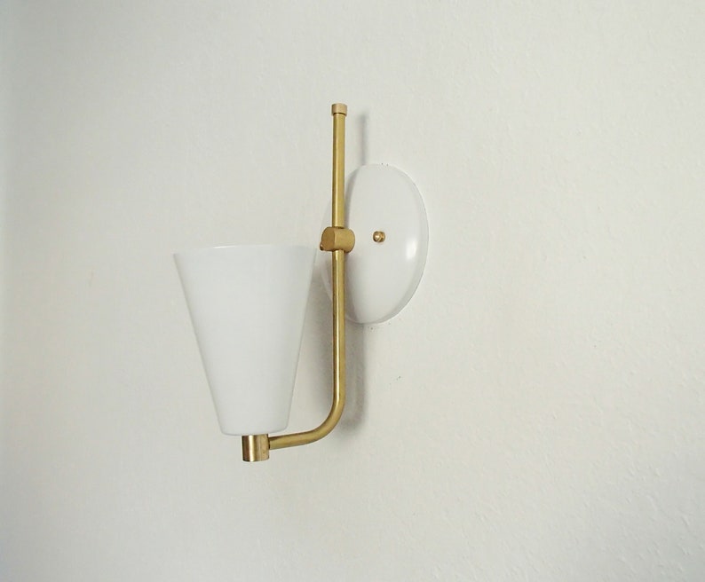 Puede incluir: Una l&aacute;mpara de pared blanca con un brazo de metal dorado y una pantalla c&oacute;nica blanca.